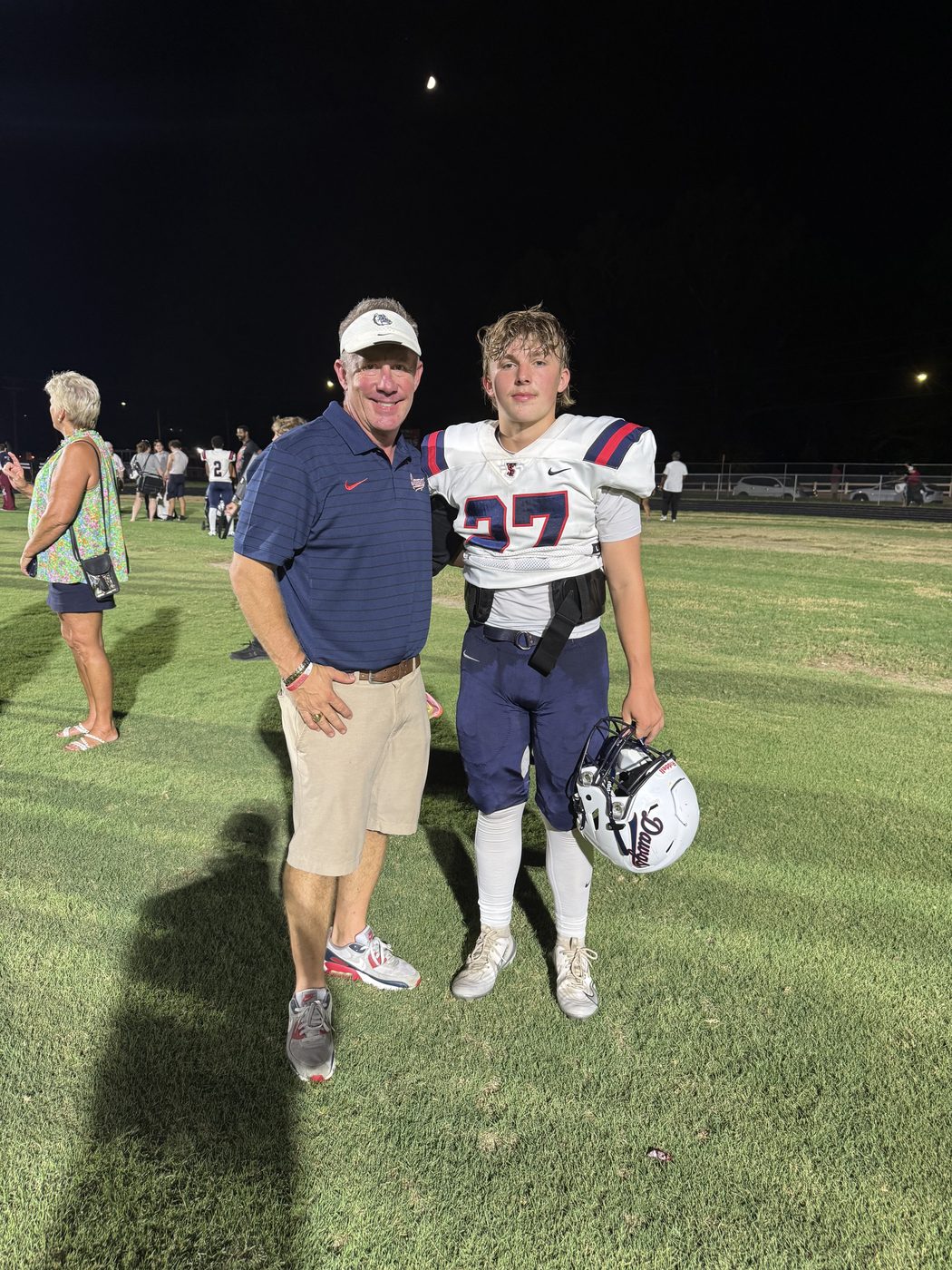 Bryan Moore standing on the field beside a Terry Sanford football player in uniform, under the stadium lights after a game.