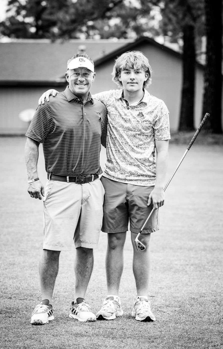 Bryan Moore with his son on a golf course, his son holding a club. Black and white photograph.
